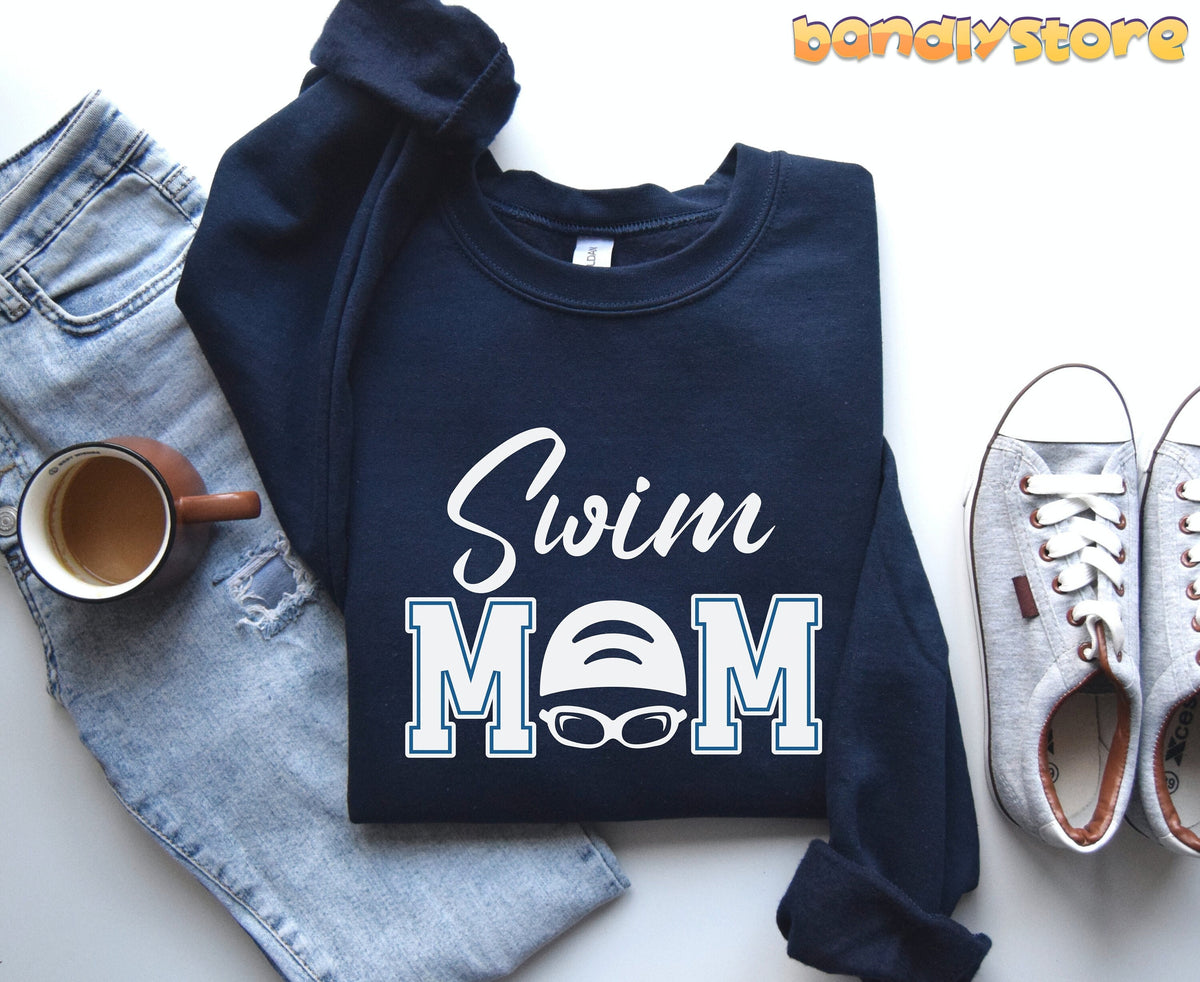 Swim Mom Sweatshirt in navy, flat-laid with jeans, a coffee mug, and grey sneakers beside it.