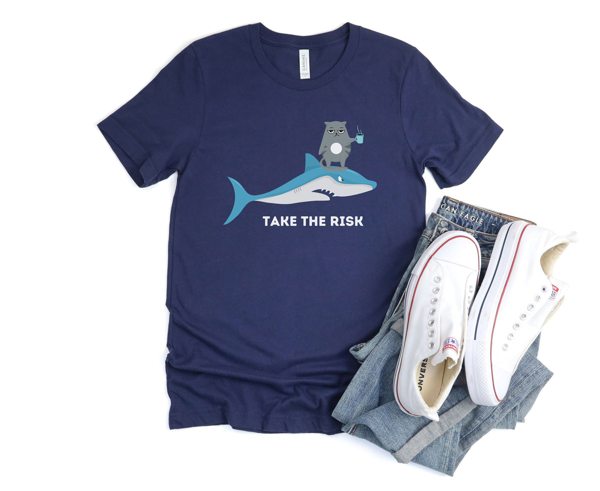 Take The Risk Funny Cat T-Shirt navy flat-laid beside folded jeans and white sneakers.