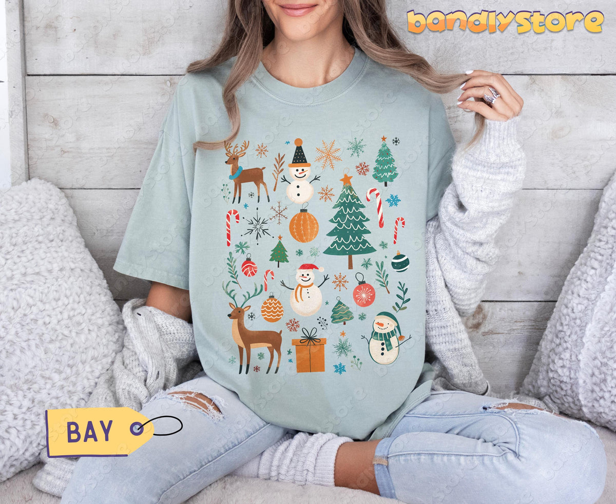 Tis The Season Christmas T-Shirt in Bay on a seated model against a wooden wall with pillows.