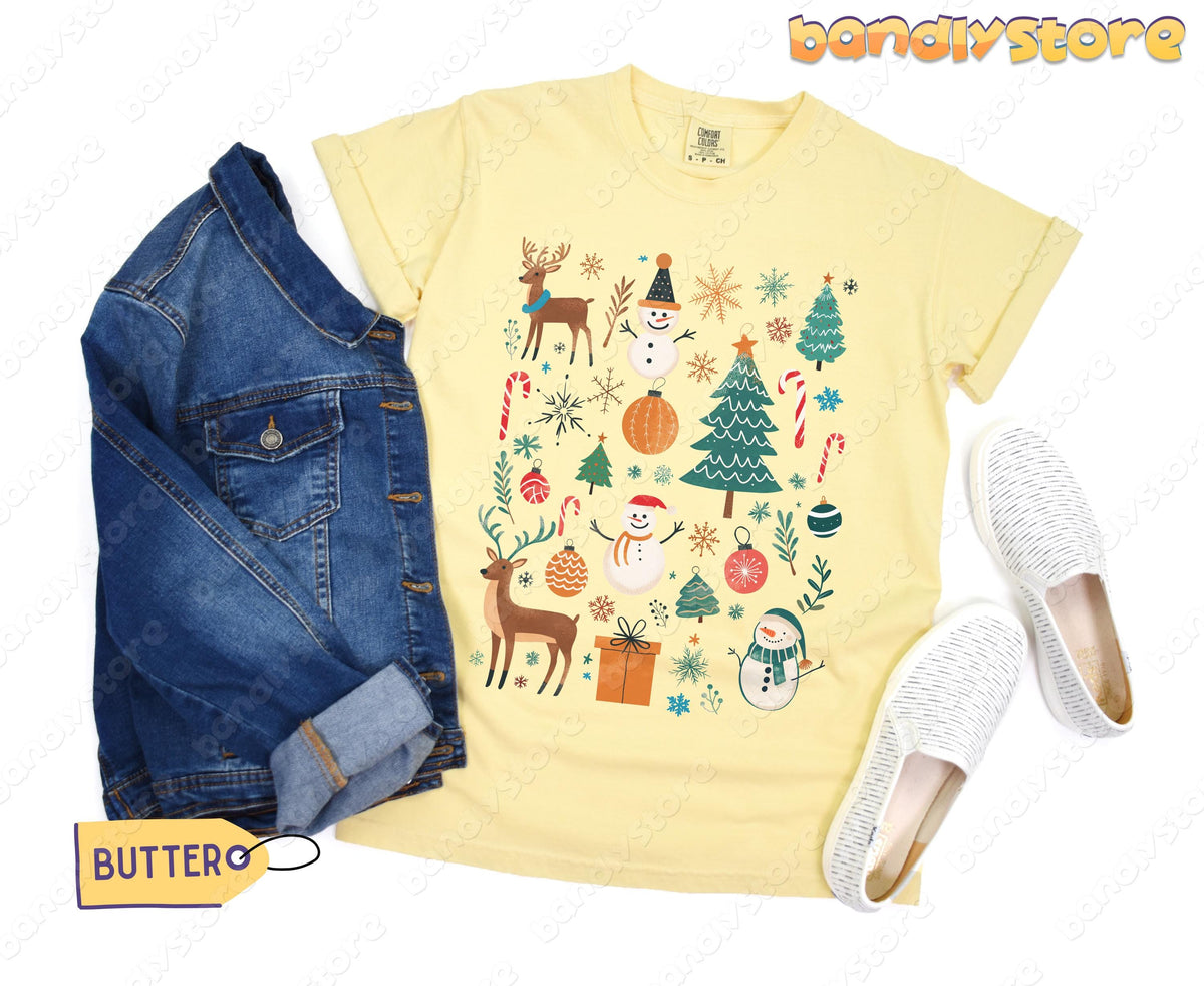 Tis The Season Christmas T-Shirt in butter flat-laid beside a denim jacket and white slip-ons.