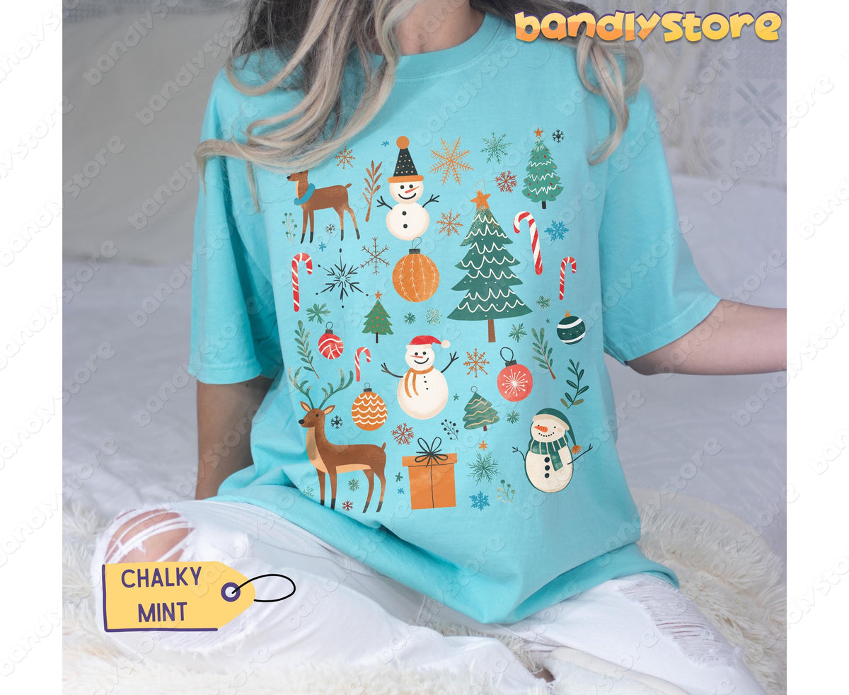 Tis The Season Christmas T-Shirt in Chalky Mint on a seated person facing forward against white fluffy bedding.