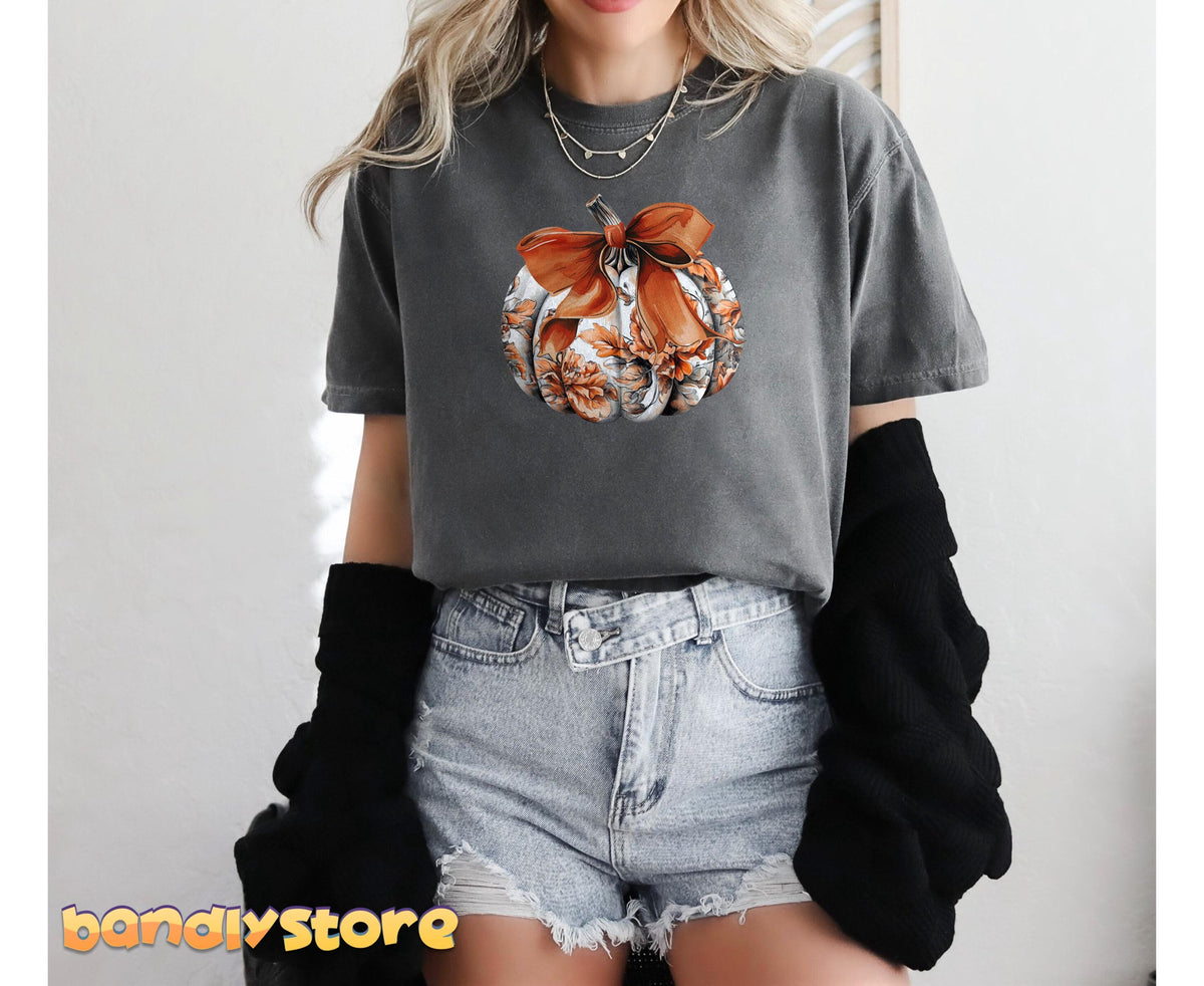 Cute Toile Pumpkin Bow T-Shirt in Pepper, worn front-facing with denim shorts and a black layer against a plain wall.