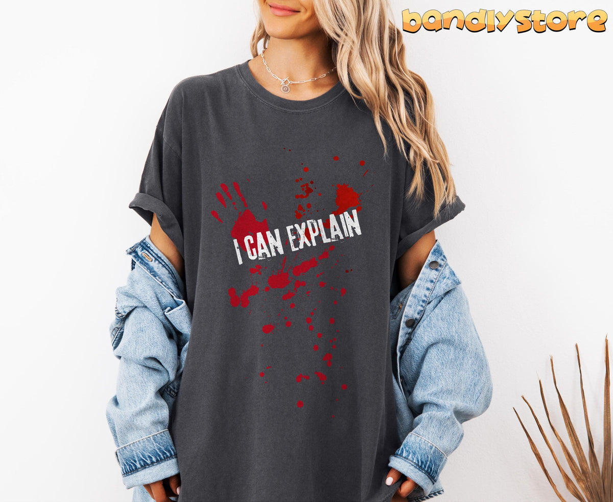 I Can Explain T-Shirt in Pepper, worn front-facing with red handprint and splatters, denim jacket and plant nearby.