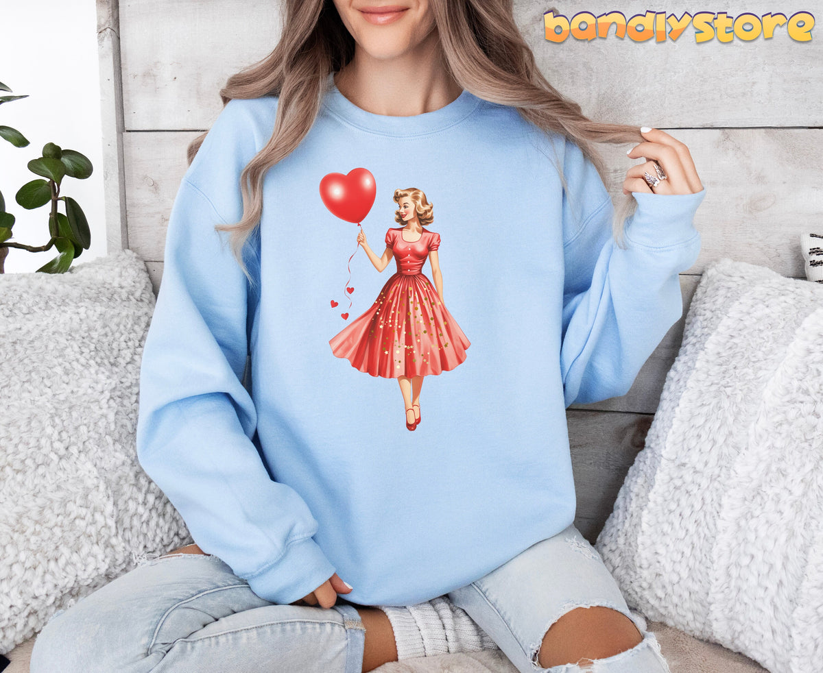 Valentine Girl Sweatshirt in light blue on a seated person against a wooden wall with pillows and a plant.