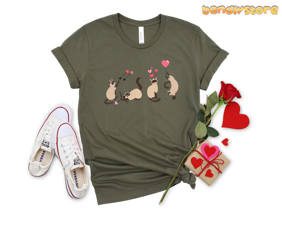 Valentine's Day Siamese Cat T-Shirt in military green shown flat from above beside sneakers, a rose and a gift box.