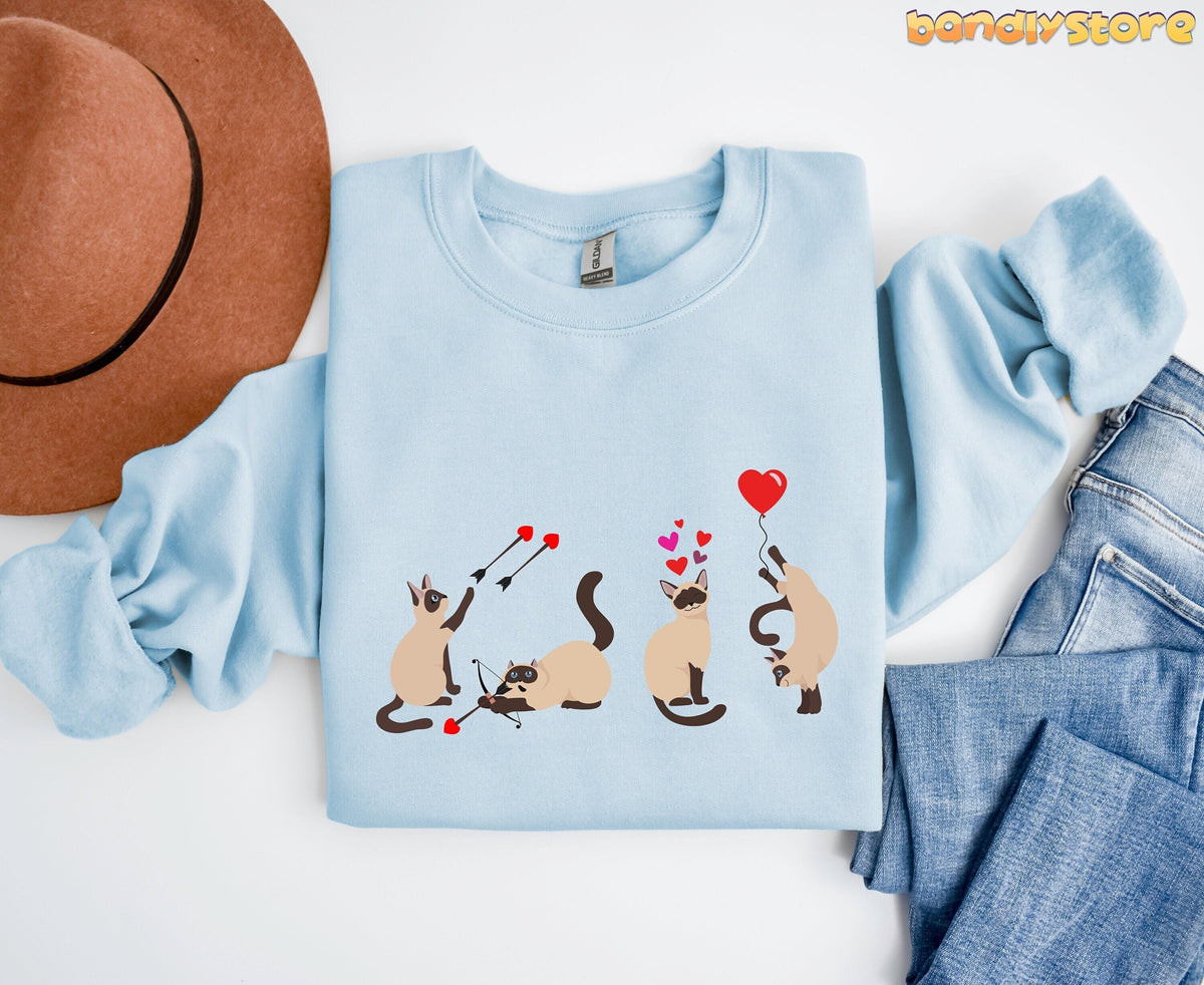 Siamese Cat Valentine Sweatshirt in light blue, folded flat beside a brown hat and blue jeans.