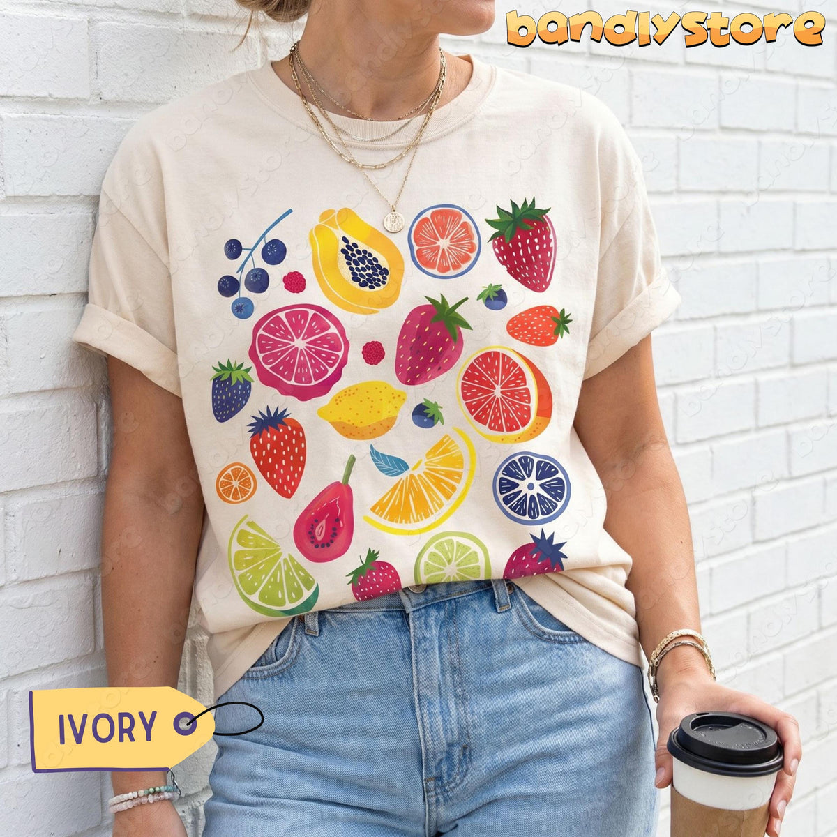 Cute Fruit T-Shirt in ivory on a person against a white brick wall holding a coffee cup.