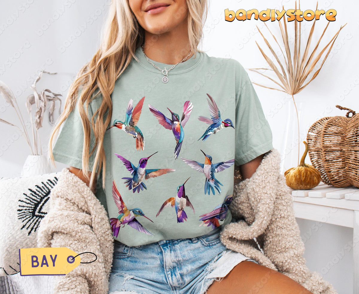 Vintage Hummingbird T-Shirt in Bay worn by a blonde woman seated indoors beside dried plants and baskets.