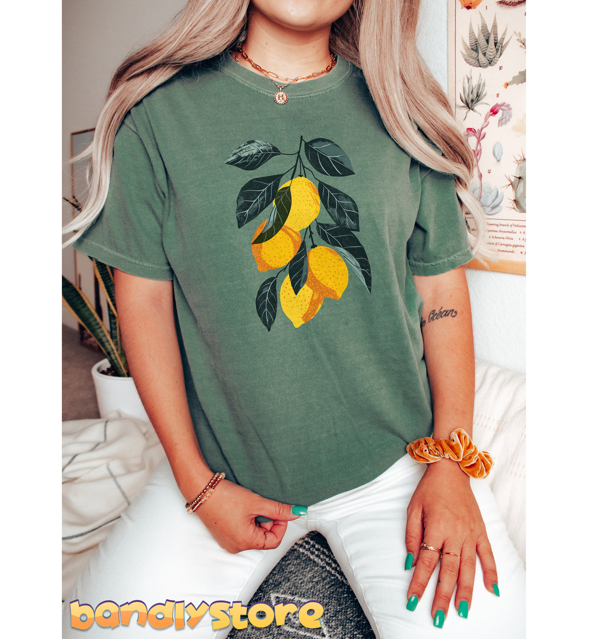 Vintage Lemons T-Shirt in moss, front view on a seated person amid plants and a botanical print.
