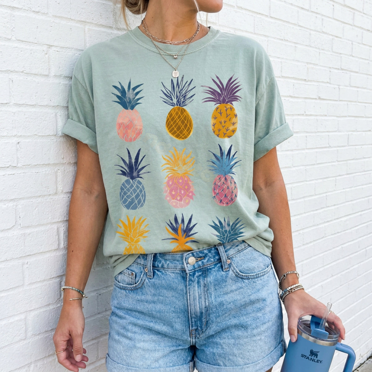 Vintage Pineapple T-Shirt in Bay, worn front-facing by a person against a white brick wall holding a blue Stanley tumbler.