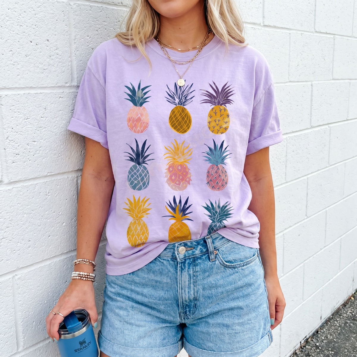 Vintage Pineapple T-Shirt in orchid worn front-facing against a white brick wall while holding a tumbler.