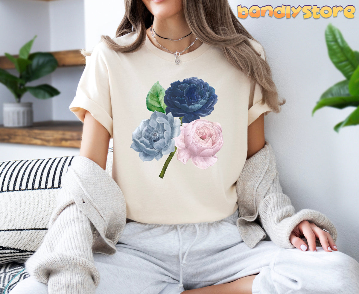 Vintage Rose Flowers T-Shirt in natural on seated woman indoors beside plants and wooden shelf.
