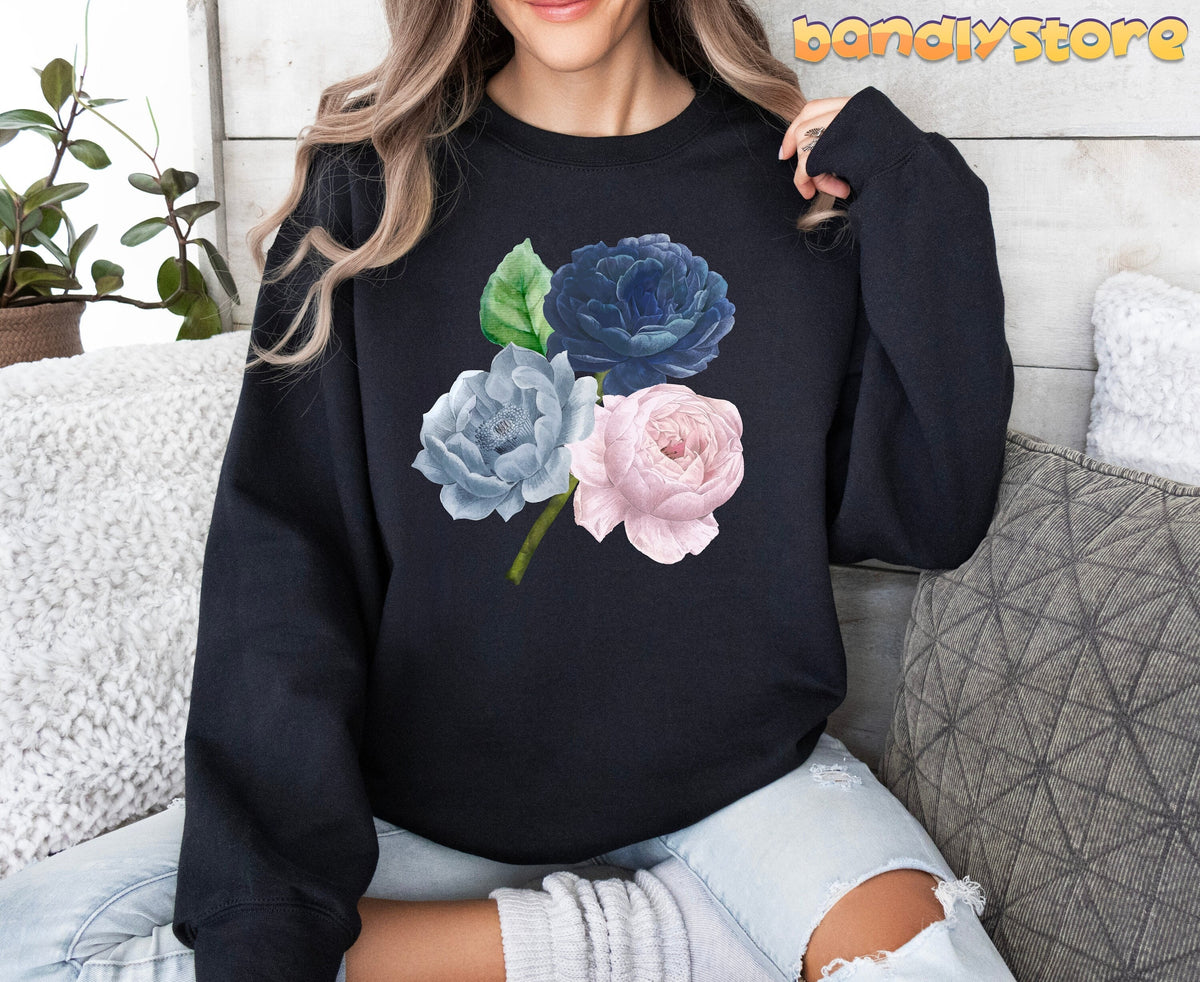 Vintage Roses Sweatshirt in black on a seated person amid pillows, plant and wood wall.