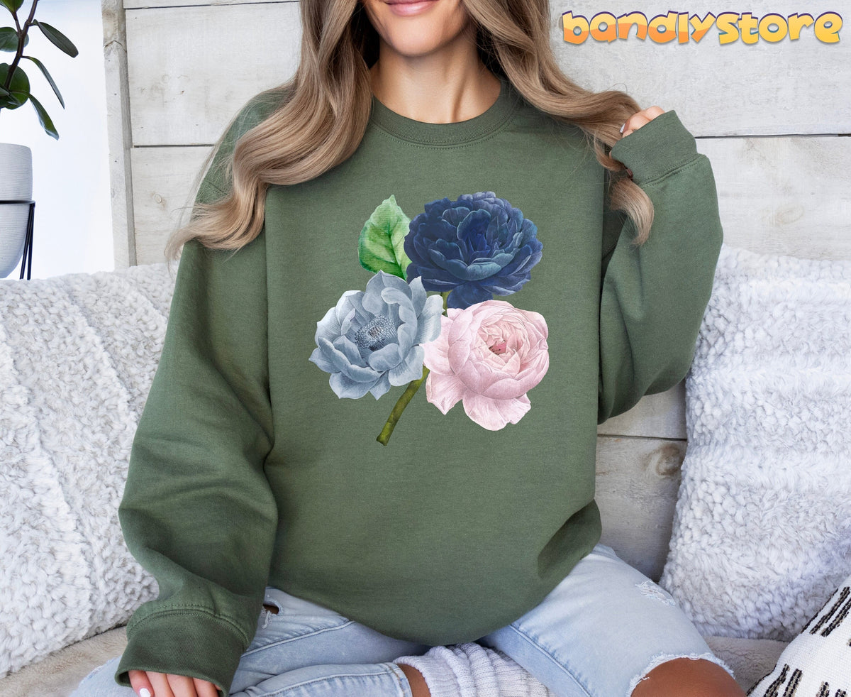 Vintage Roses Sweatshirt in military green on a woman seated amid white pillows by a wood wall.