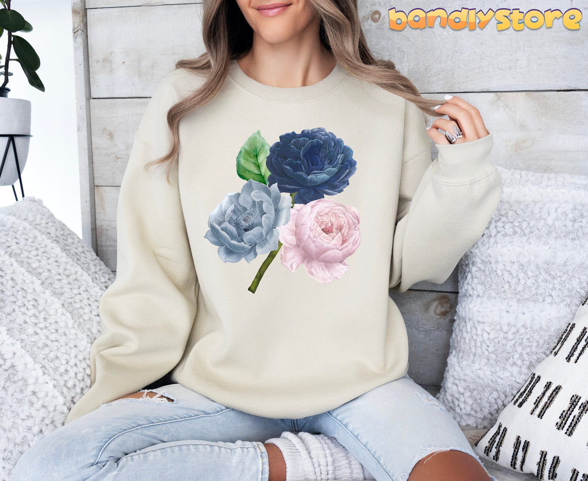 Vintage Roses Sweatshirt in sand, worn by a seated woman amid pillows against a wood wall.