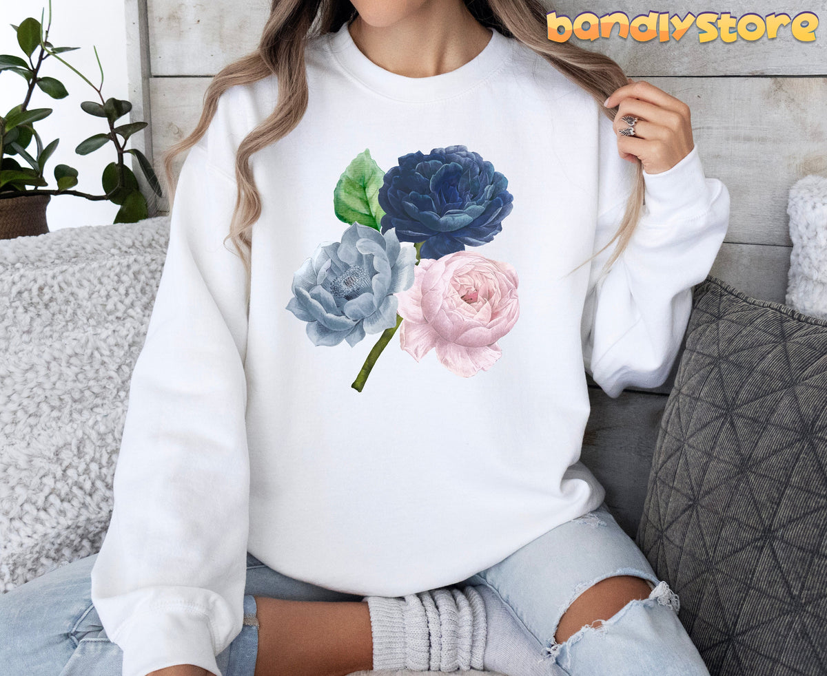 Vintage Roses Sweatshirt in white on seated person beside plant and pillows, front view.
