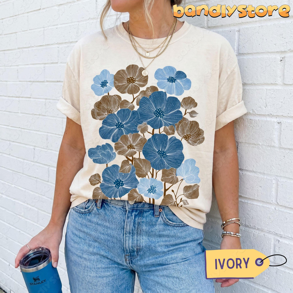 Vintage Wildflowers Linocut T-Shirt in ivory on a person against a white brick wall holding a blue tumbler.