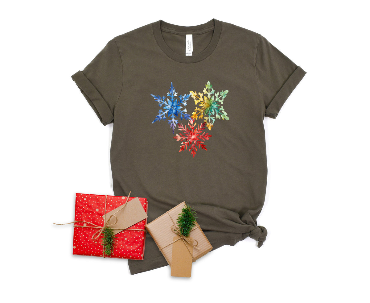 Colorful Watercolor Snowflakes T-Shirt in Army, flat-laid with rolled sleeves and hem knot beside two twine-tied gift boxes.