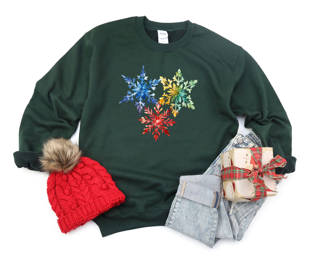 Colorful Watercolor Snowflakes Sweatshirt in forest green flat-laid with red beanie, jeans and gift.