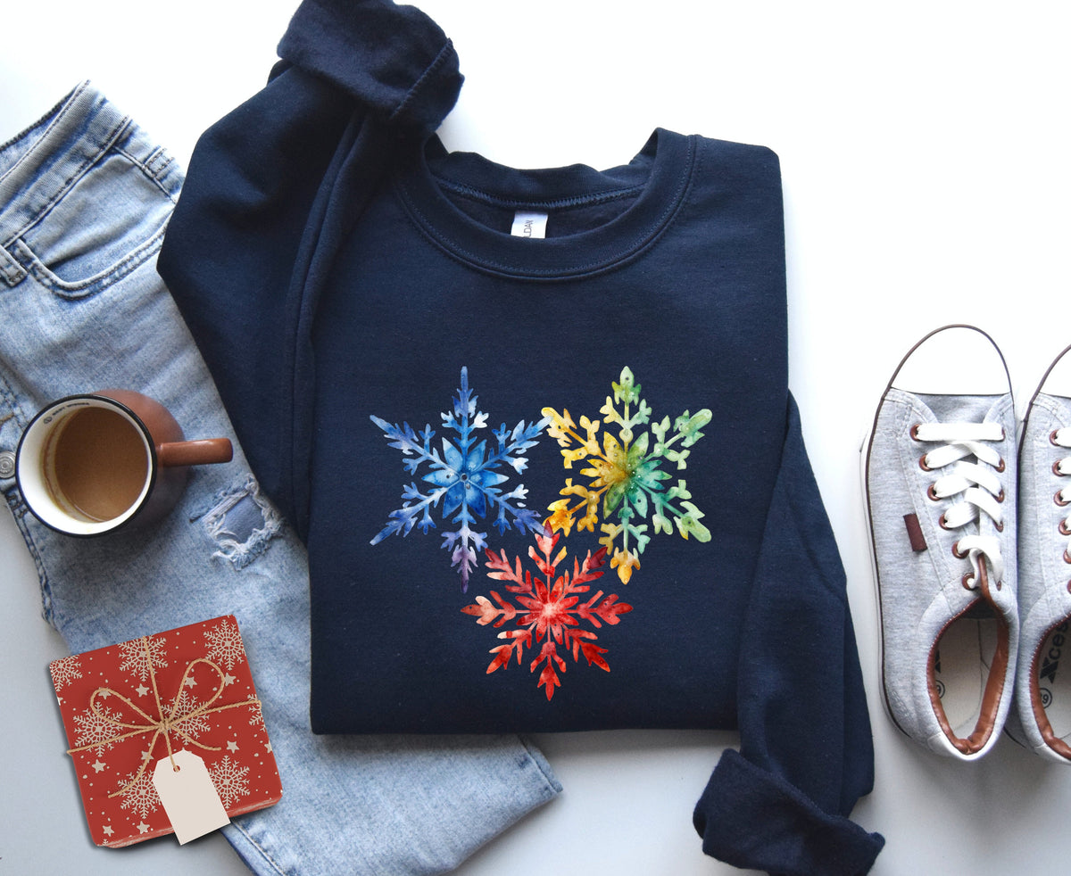 Colorful Watercolor Snowflakes Sweatshirt in navy flat-laid with jeans, mug, gift box and sneakers around it.