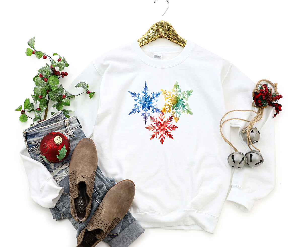 Colorful Watercolor Snowflakes Sweatshirt in white on a gold hanger beside holly, jeans, boots and jingle bells.