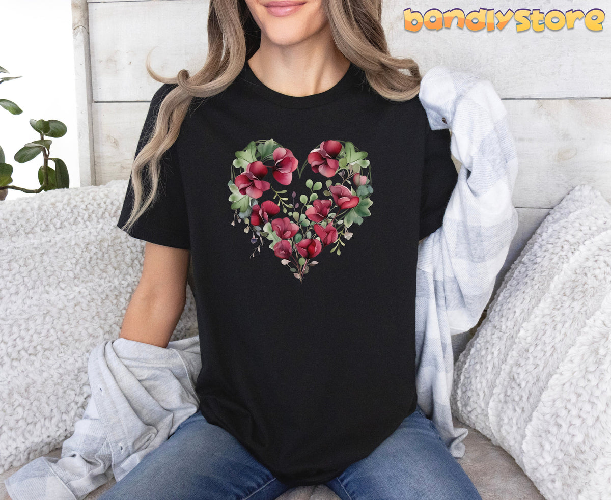 Watercolor Sweet Pea Heart T-Shirt on black fabric, modeled seated amid white cushions and greenery.