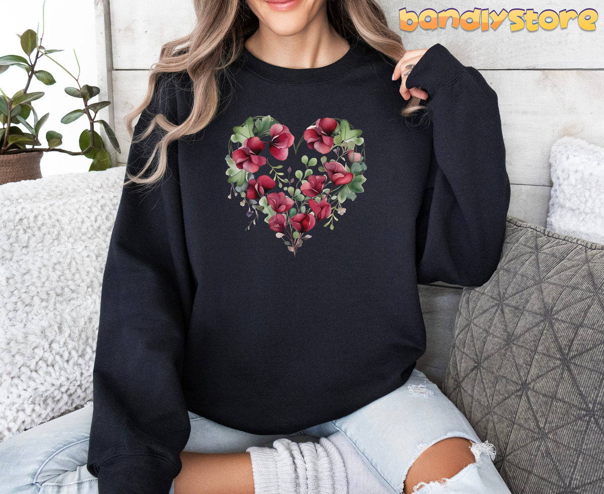 Watercolor Sweet Pea Heart Sweatshirt in black on a person sitting indoors with pillows and a plant.