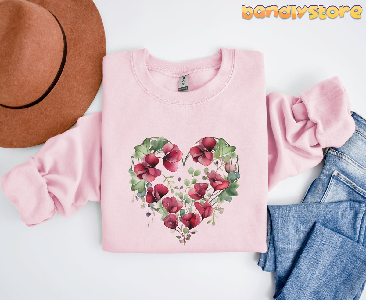 Watercolor Sweet Pea Heart Sweatshirt in light pink flat-laid beside a brown hat and blue jeans.