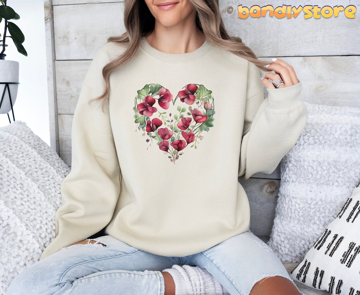 Watercolor Sweet Pea Heart Sweatshirt in sand, front view on seated model amid pillows, plant, and wood wall.